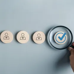 image of wooden tiles with images of employees on each and magnifying glass over a checkmarked tile illustrating the idea of management by exception