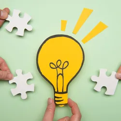 illustration of a lightbul with hands around it holding puzzle pieces illustrating the concept of the benefits of brainstorming