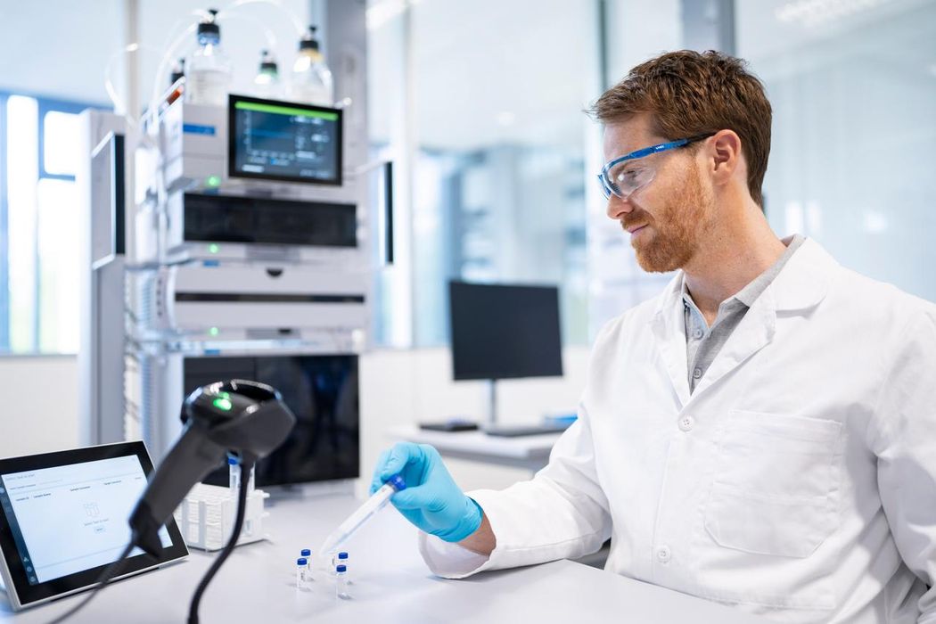 Male scientist in safety glasses and a white lab coat scans the labels on test tubes with a barcode scanner