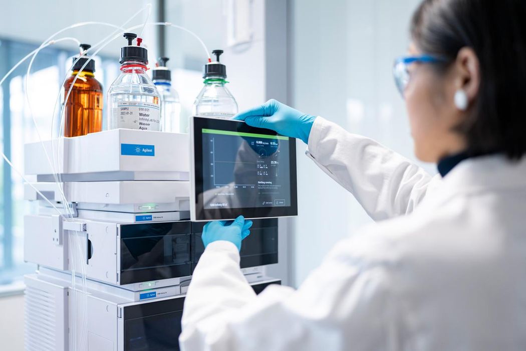 Female scientist in safety glasses and a white lab coat uses a liquid chromatography system