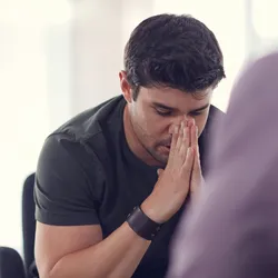 image of a sad looking employee with eyes closed and hands folded illustrating theimportange of managing grief in the workplace