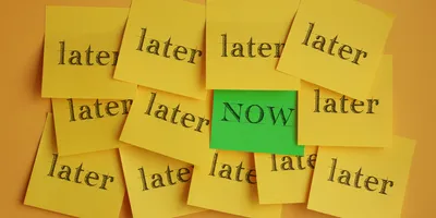 image of a group of yellow post-it notes on a wall all reading "later" with one green note that says "now" illustrating the concept of overcoming procrastination