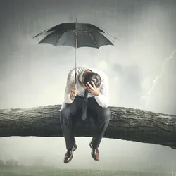 a man sits on a branch looking despondent holding an umbrella agaist a storymy sky illustrating the concept of failing as a manager