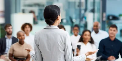 image of a woman from behand presing to an audience of seated people illustrating the benefits of effective employee training