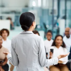 image of a woman from behand presing to an audience of seated people illustrating the benefits of effective employee training