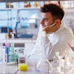 lab technician setting in a lab with hand on chin looking disengaged illustrating the concept of bored employees being disgruntled at work