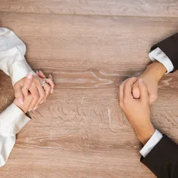 image of hands folded on a boardroom table opposite each other and suggesting the benefits of heatly workplace conflice