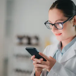 a yourng woman in a lab coat using a cell phone and illustrating the dangers of using cell phones in the laboratory