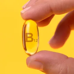 Close-up shot of a person holding a large yellow vitamin that says B12 on it