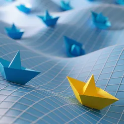 image of a yellow paper boat on a way surface followed by several blue boats illustrating the concept of leading versus managing