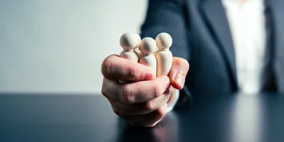 manager holding wooden figures of people gripped tightly in thier fist illustrating the concept of autocratic leadership style