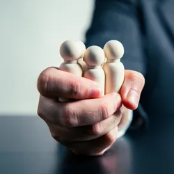 manager holding wooden figures of people gripped tightly in thier fist illustrating the concept of autocratic leadership style