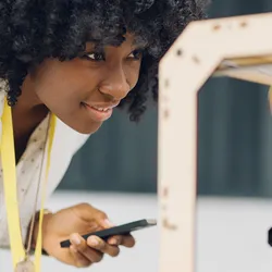 A young engineer closely examines a 3D printer as it fabricates a complex blue geometric structure, highlighting advancements in thermoelectric materials and cooling applications.