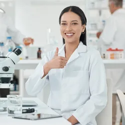 Young woman working in a lab smiling and give a thumbs upp suggesting the imprtance of improving job satisfaction and productivity