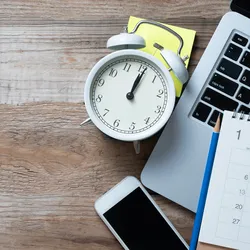 image of an alarm clock on a desk with phone papers and a laptop illustrating the concept of effective time management
