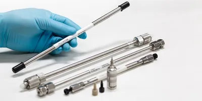 a series of hplc columns on a white background with a gloved hand holding a single column illustrating the importance of chromatography column safety in the lab