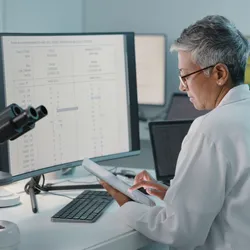 image of a scientist working with a tablet and computer illutrating the idea of manual versus automated data reporting
