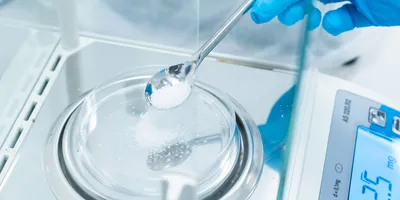A gloved hand scooped a white substance onto a tray sitting on a balance