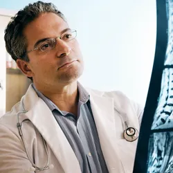 A doctor in a white coat examines a spinal X-ray, analyzing the vertebrae for potential injuries. Advances in robotics and spinal stimulation offer hope for restoring movement in paralysis.