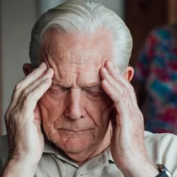 An elderly man rubs his temples with his eyes closed