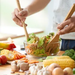 Person preparing fresh vegetable salad surrounded by colorful produce, promoting healthy eating in midlife.