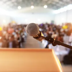 microphone and podium in front of a large audience of people illustrating the importance of becoming a good public speaker