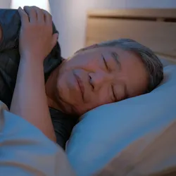 Older man sleeping peacefully in bed, illustrating connection between Alzheimer’s and sleep