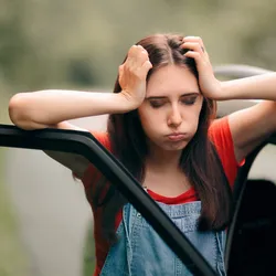 Young woman looking nauseous beside a car, representing need for sound therapy for motion sickness.