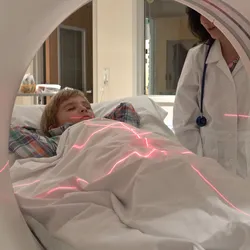 Young patient undergoing CT scan with laser alignment as doctor supervises the procedure.
