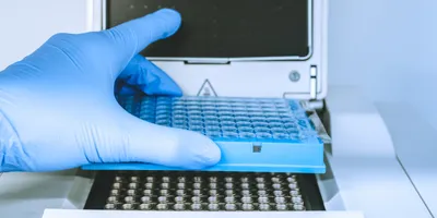 Research scientist putting test 96 well platte into real-time pcr machine.