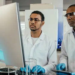 Two scientists in lab coats and gloves analyzing data on a computer in a modern laboratory