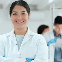 Confident female scientist smiling in lab with team collaborating in the background.