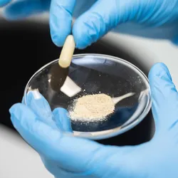gloved hands holding a glass dich containing a pharaceutical capule and powder illutrating the significance of testing for genotoxic impurities in the pharaceutical industry