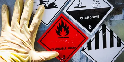 Gloved hand upon a container with multiple hazard signs on it.