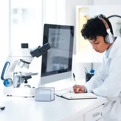 Lab worker wearing headphones for noise reduction while writing in a notebook