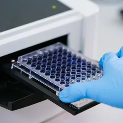 Scientist placing a 96 well plate into a microplate reader.