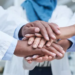 Close-up of diverse laboratory staff in white lab coats placing their hands together, symbolizing teamwork and trust, which is essential for emotional express to build lab collaboration
