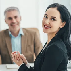 Lab manager advocacy for investment in the lab. A confident professional woman smiling in a business meeting, with a man holding a YES sign in the background.