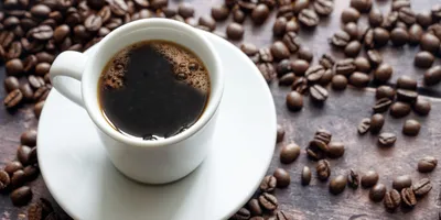 A cup of coffee surrounded by coffee beans signifying caffeine boosting mitochondria.