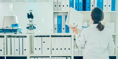 Female in lab coat utilizing record keeping for GMP.