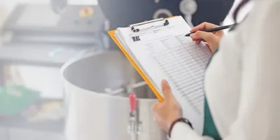 Lab worker holding a clipboard and pen, symbolic of preparing the lab for regulatory inspections.