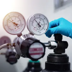 Lab technician adjusting a gas cylinder regulator—illustrates supply risk in helium-based GC workflows