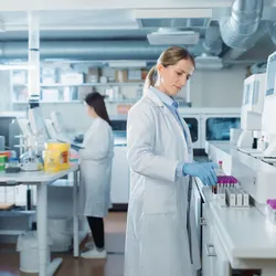 Scientists in a clean laboratory handling test tubes under GMP-compliant conditions.