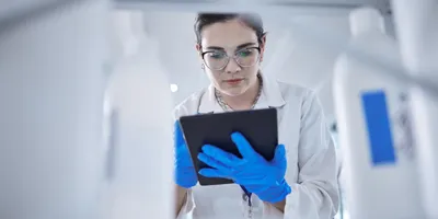 Scientist in lab coat and gloves using a tablet for chemical inventory management.