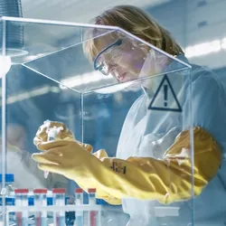 A scientist wearing elbow-length gloves prepares samples under a vented workspace like a glove box