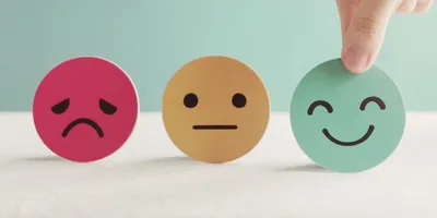 Three face icons showing a sad, neutral, and happy expression, with a hand selecting the happy one—symbolizing how lab managers can influence mental health at work.