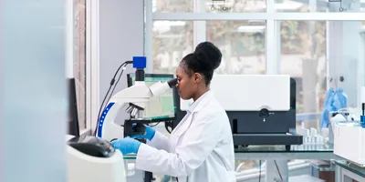 Lab technician using a microscope at a bench workstation—highlighting ergonomic posture and equipment setup for preventing injury.