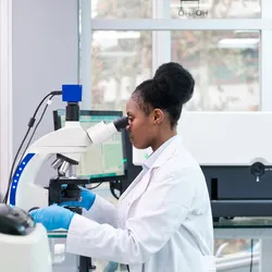 Lab technician using a microscope at a bench workstation—highlighting ergonomic posture and equipment setup for preventing injury.