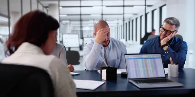 Frustrated office team in a meeting showing signs of stress and disengagement due to demotivating behaviors.