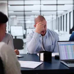 Frustrated office team in a meeting showing signs of stress and disengagement due to demotivating behaviors.